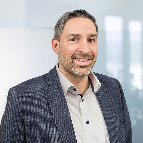 Portrait von Markus Mohr. Er lächelt in die Kamera und steht seitlich