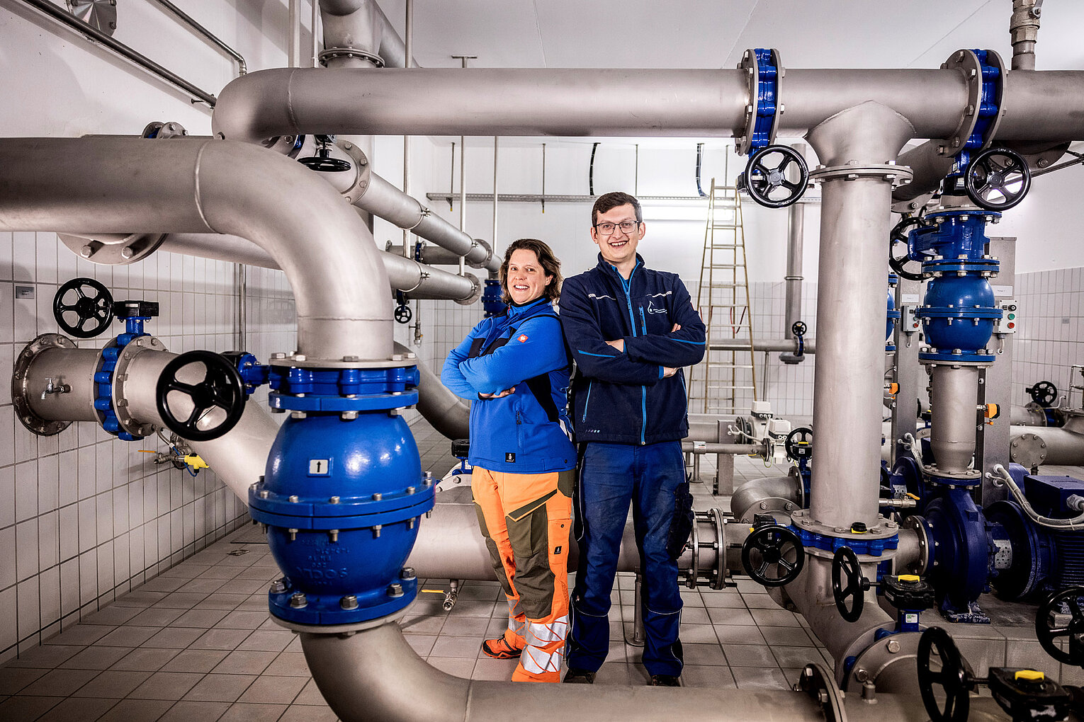 Technikraum vor Ort Mitarbeitende im Technikraum mit blauen Rohrleitungen und Anlagen